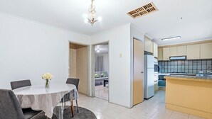 A modern kitchen with a built-in stove, refrigerator, and a small dining area with a table and chairs. - Well-Located St Albans Stay with Fully Equipped Kitchen (Saint Albans)