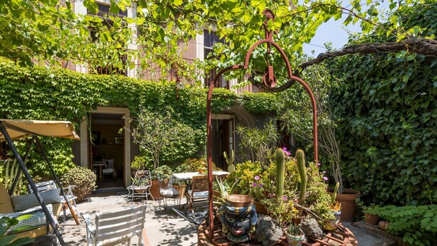 An outdoor patio with a brick planter, chairs, tables, and potted plants.