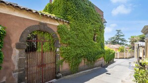 A narrow street with a building covered in green ivy, a metal gate, and a clear blue sky.
