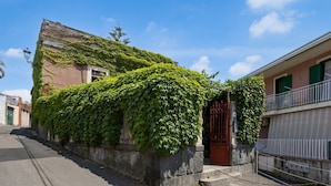 A building with a stone wall and a metal gate, surrounded by greenery.