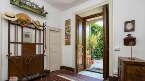 A hallway with a patterned rug, a mirror, hats on a stand, and a door leading outside.