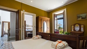 A hotel room with a large bed, a wooden wardrobe, a mirror, and a window with a view.
