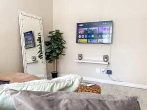 A bedroom with a bed, a mirror, a potted plant, a TV mounted on the wall, and a small wooden stool. - Cozy 1-bedroom apartment in charming Cape Town with AC (Cape Town)