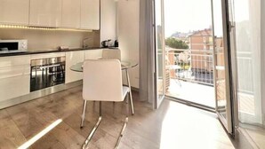 Una cocina moderna con armarios blancos, una mesa de comedor de vidrio y un puerta corrediza de cristal que da a un balcón.