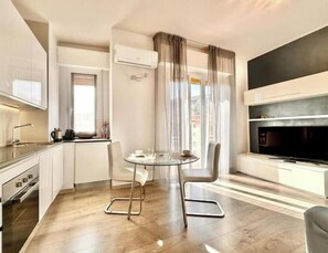 A modern kitchen with a dining area, a TV, and a window with curtains. - Hostdomus - Blanca Suite (Finale Ligure)