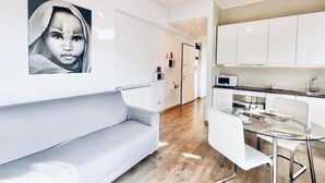 Una sala moderna con un sofá, una mesa de comedor de cristal y armarios blancos.