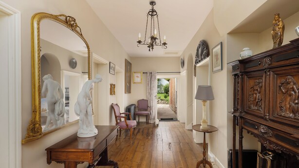 A hallway with a large mirror, wooden furniture, and a chandelier.
