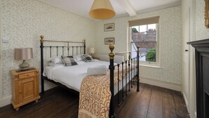 A bedroom with a bed, wooden nightstand, lamp, and a window with a view of a brick building.