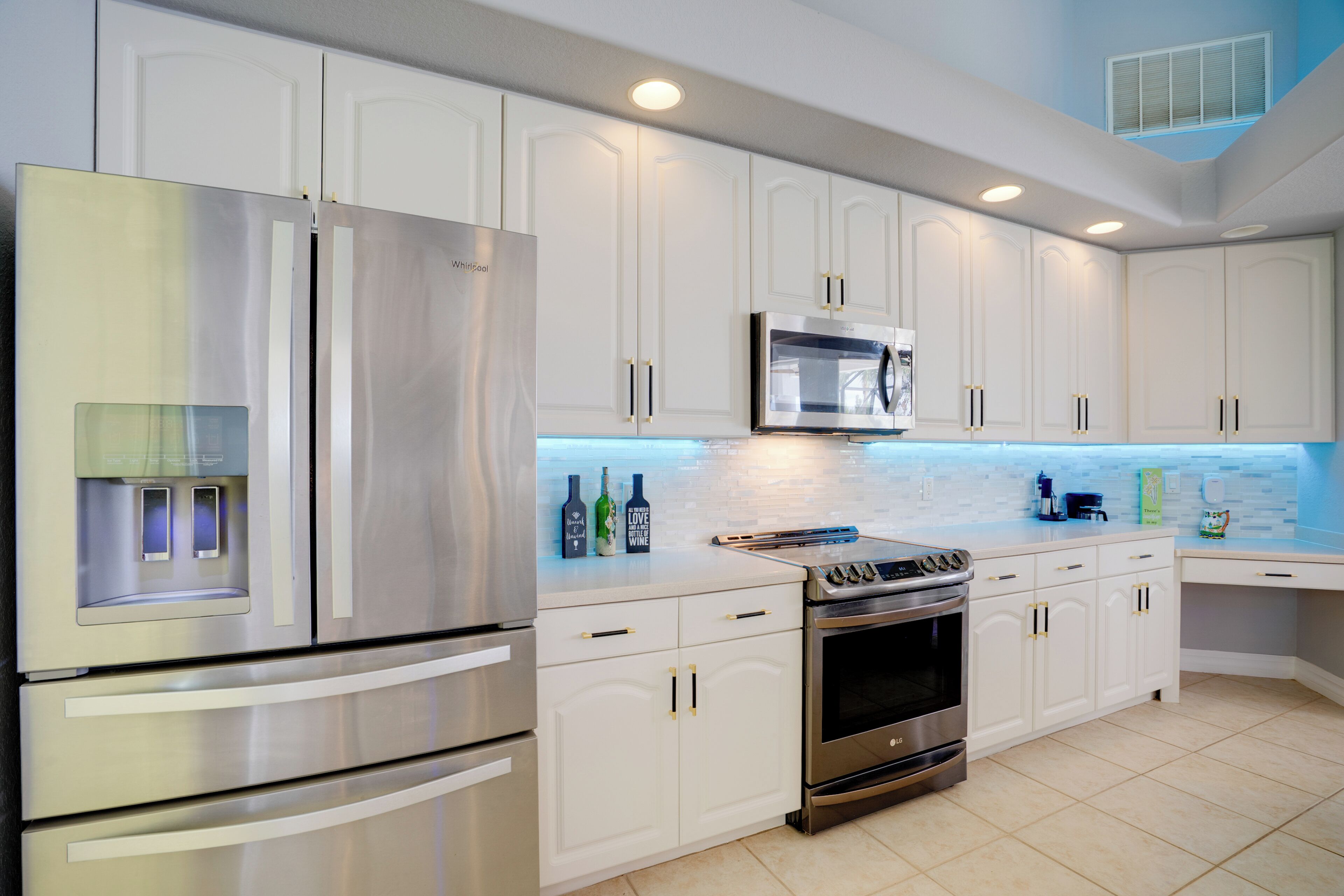 Una cocina moderna con electrodomésticos de acero inoxidable, armarios blancos y salpicadero azul.