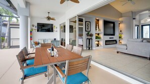 A spacious living area with a dining table, chairs, ceiling fans, a TV, and a sofa. - Cape Coral Lakefront Living! Home w/ Pool, Lanai (Cape Coral)