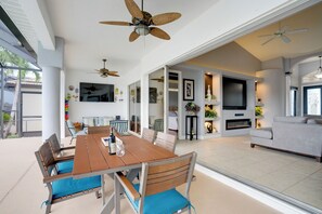A spacious living area with a dining table, chairs, ceiling fans, a TV, and a sofa. - Cape Coral Lakefront Living! Home w/ Pool, Lanai (Cape Coral)