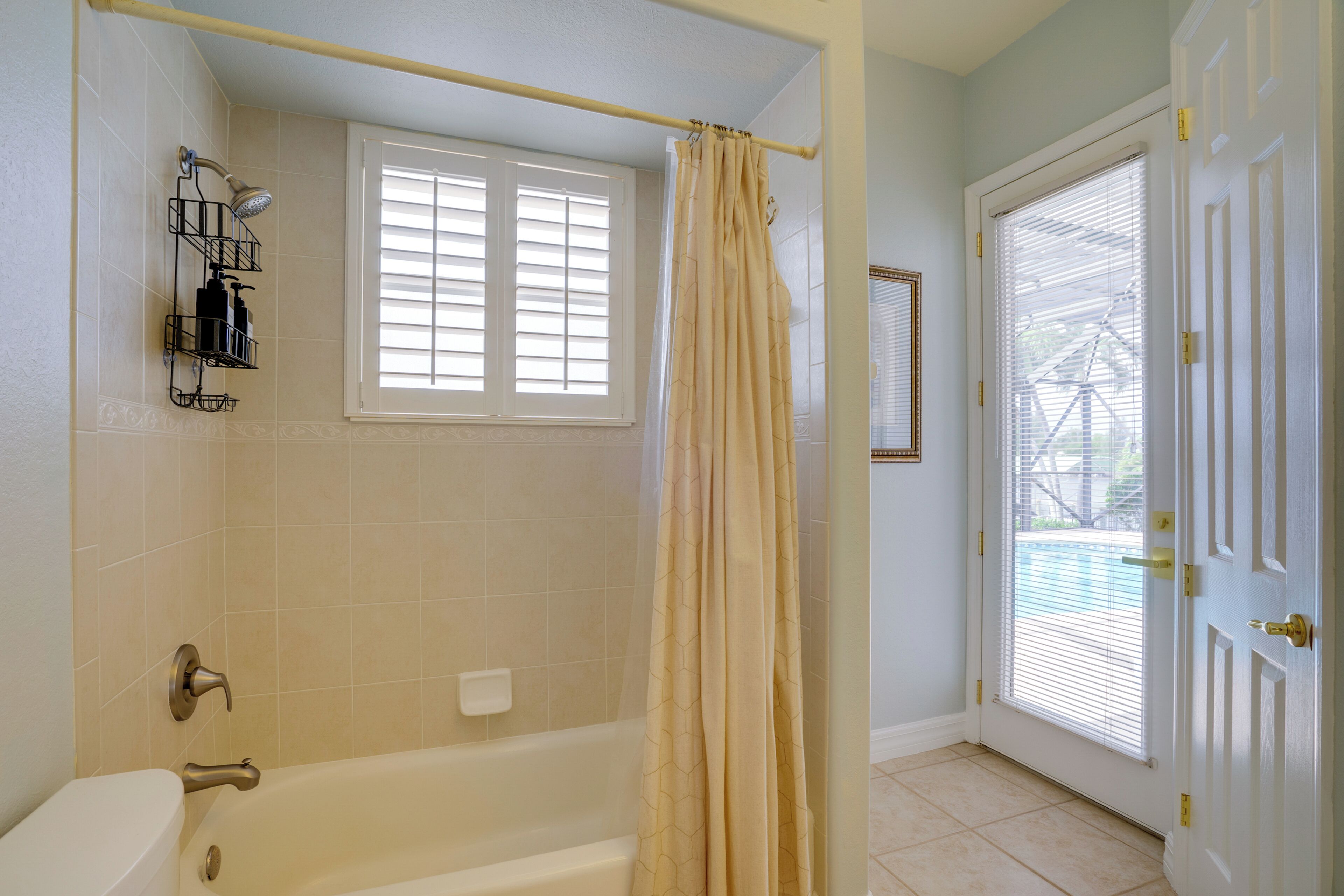 A bathroom with a bathtub, a window with blinds, a shower curtain, and a door with a window.