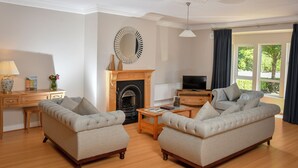 A living room with a fireplace, two sofas, a coffee table, a TV, and a desk with a lamp.
