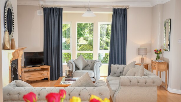 A living room with a sofa set, a television, a fireplace, and a view of greenery outside.