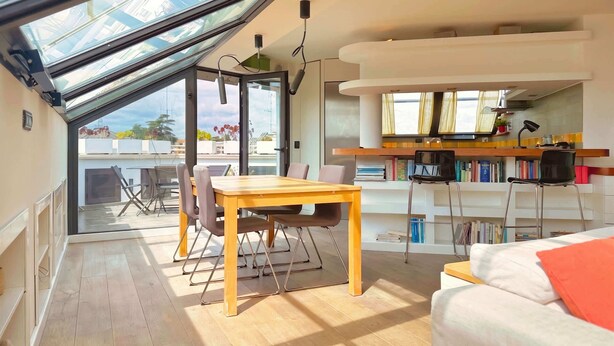 Et moderne interiør med et spisebord, en sofa, en reol og et ovenlys.