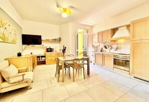 Eine moderne Küche mit Holzausstattung, einem Essbereich mit Tisch und Stühlen, einem Fernseher an der Wand und einem Deckenventilator.