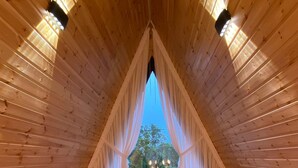 A cozy, triangular wooden room with a bed, pillows, and a view through a window.