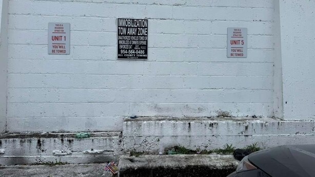 Un muro de ladrillo blanco con tres señales de zona de remolque para las unidades 1, 2 y 5.