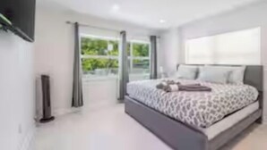Un dormitorio moderno con una cama grande, un televisor de pantalla plana y un ventanal corredero al exterior.