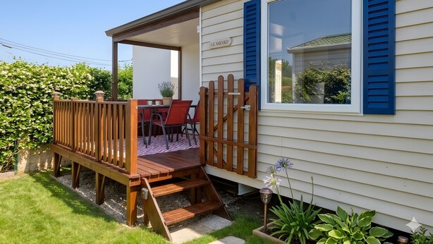 A mobile home with a deck, a dining area, and a window with shutters.