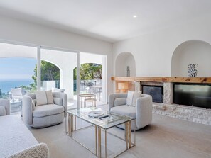 Ein modernes Wohnzimmer mit einem Glastisch, zwei grauen Sofas, einem Kamin und einem an einer Steinwand montierten Fernseher.