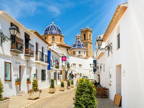 A narrow cobblestone street lined with white buildings, some with balconies and potted plants. - Preciados by Interhome (Altea)
