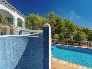 A swimming pool with a tiled edge, surrounded by potted plants and a white building with arches. - Preciados by Interhome (Altea)