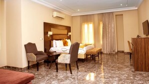 Habitación de hotel con cama, dos sillones, escritorio, televisor y suelo de mármol.