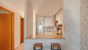 A kitchen with white brick walls, wooden cabinets, a stainless steel refrigerator, and two wooden stools. - Duplex with sea view (Adeje)