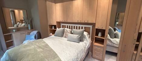 Un dormitorio con cama, armario de madera y espejo.
