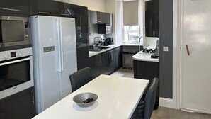 Una cucina moderna con zona pranzo, caratterizzata da elettrodomestici in acciaio inossidabile, un piano di lavoro bianco e vista sull'esterno.