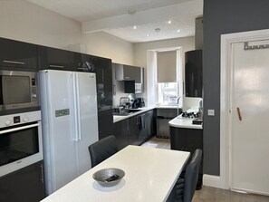 Una cocina moderna con comedor, que incluye electrodomésticos de acero inoxidable, una encimera blanca y vistas al exterior.