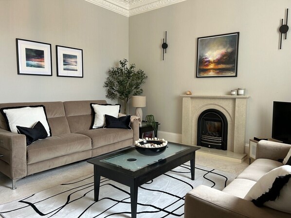 A living room with a sofa, coffee table, fireplace, and framed artwork.