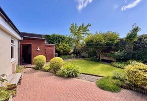 A residential property with a paved driveway, a wooden door, and a well-maintained garden with various shrubs and a lawn.