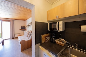Une petite pièce comprenant un lit, un coin cuisine, une télévision et une fenêtre avec des rideaux.