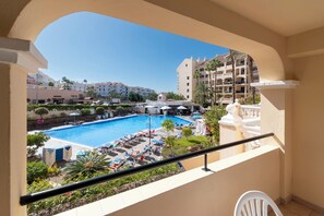 A pool area with lounge chairs and umbrellas, surrounded by greenery and buildings. - Lovely 1 Bedroom Apartment. Communal Heated Pool (CN)