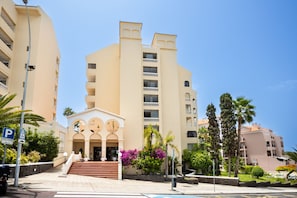 A multi-story hotel with a central entrance, balconies, and surrounding greenery. - Lovely 1 Bedroom Apartment. Communal Heated Pool (CN)