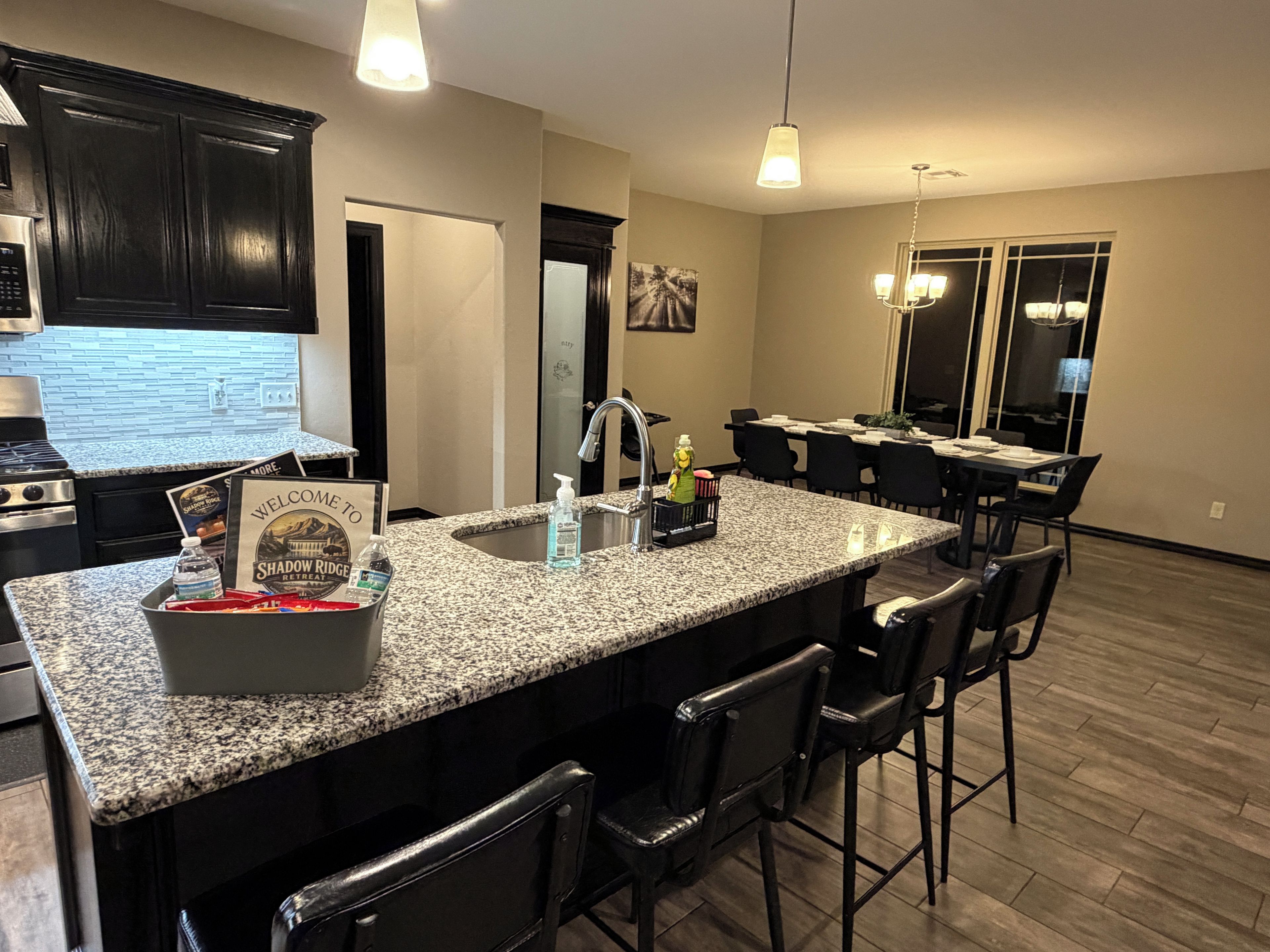 A kitchen with granite countertops, black bar stools, and a dining area with a table and chairs.