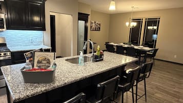 A kitchen with granite countertops, black bar stools, and a dining area with a table and chairs.
