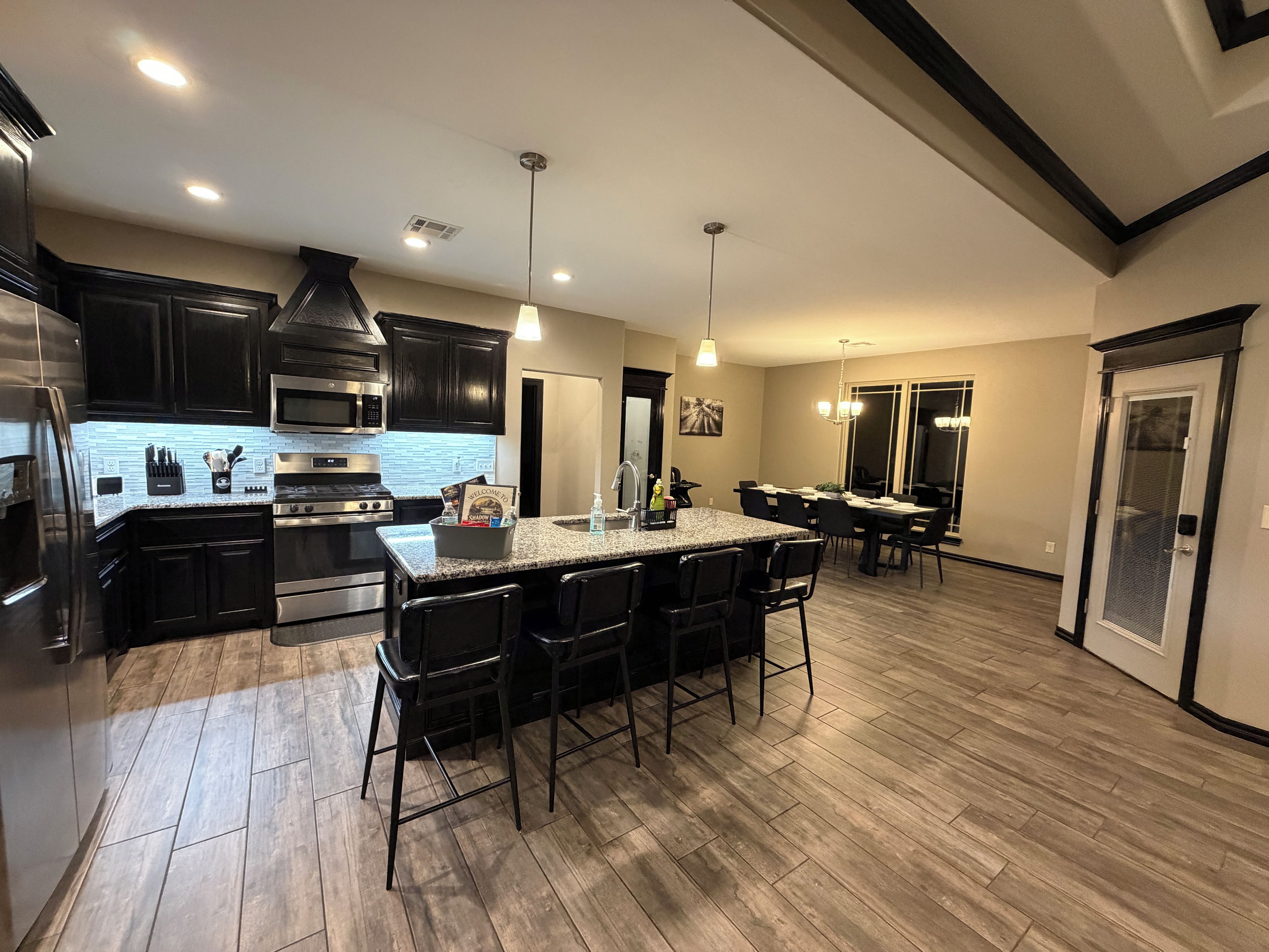 A modern kitchen with dark cabinetry, a granite countertop, and a central island with bar stools.