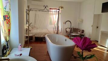 Una camera da letto con una vasca da bagno ampia, un letto a baldacchino, un tavolino con un bollitore e un termosifone.