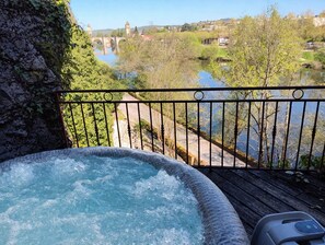 Un jacuzzi en una terraza de madera con vista a un río y un puente al fondo.