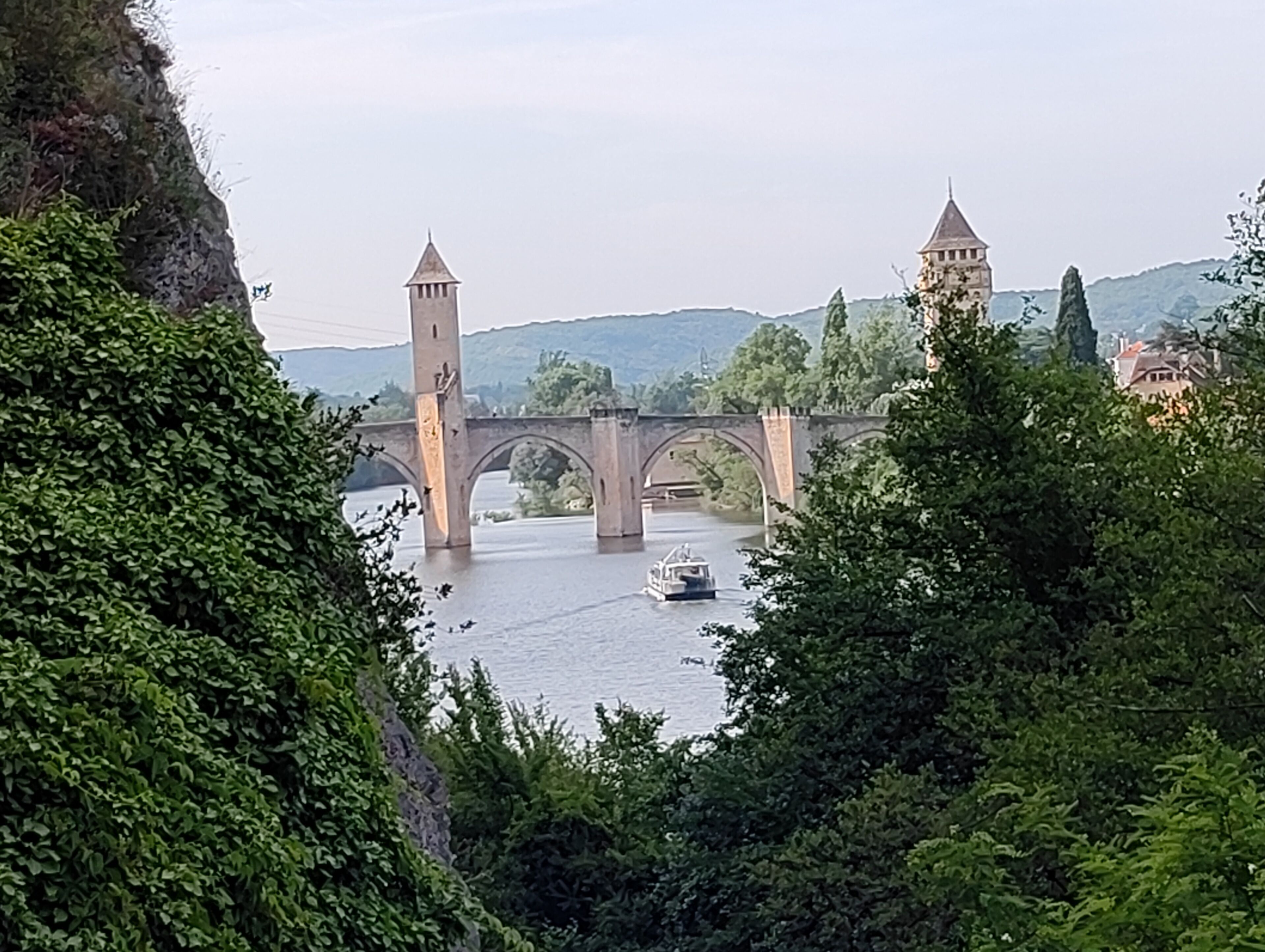 A stone bridge with towers, a river, and surrounding greenery.