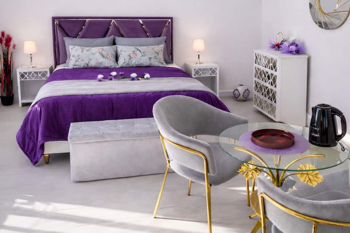 A bedroom with a bed, bedside tables, a chair, a glass table, and a chandelier.