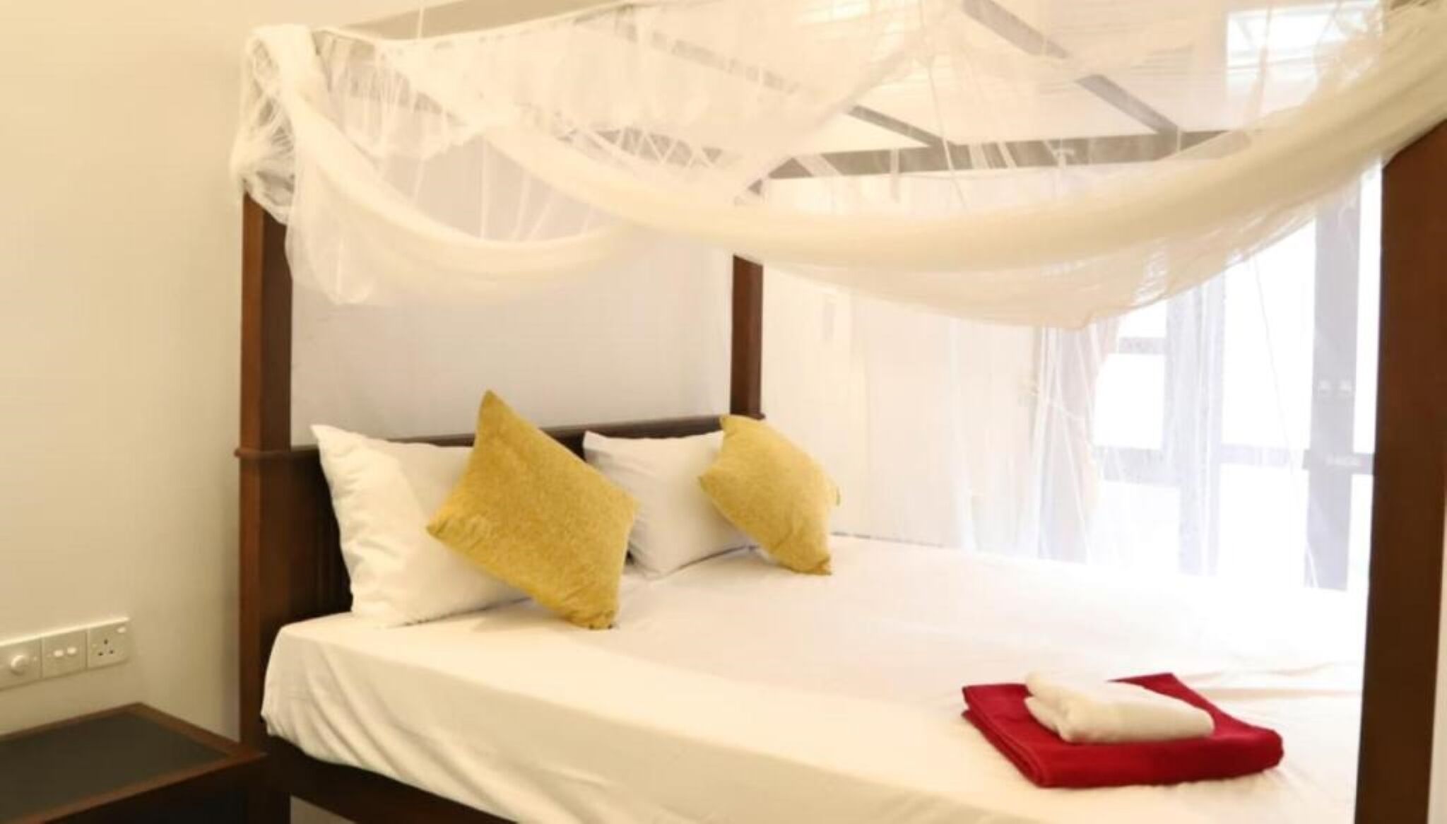 A bed with a canopy, white pillows, and a red towel.