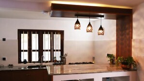 Una cocina moderna con una isla central, luces colgantes y un amplio ventanal con persianas verticales.