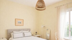 Une chambre à coucher comprenant un lit, des tables de chevet, une lampe, une chaise, un miroir et un luminaire suspendu.
