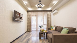 A modern living room with a sofa, a coffee table with fruits, a TV mounted on the wall, and a large window with curtains. - Stay Inn on Yekmalyan  (Yerevan)