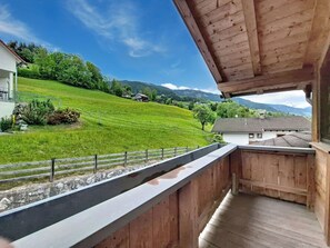 Ein Balkon mit Blick auf einen grünen Hang, eine Steinmauer und ein Gebäude mit einem geneigten Dach.