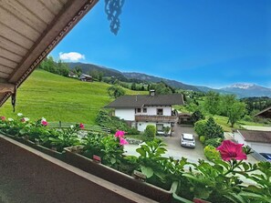 Ein Haus mit Balkon, umgeben von Grün und einer Berglandschaft.